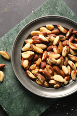 Plate with tasty Brazil nuts on black background