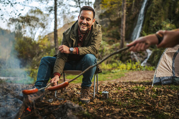 man hiker enjoy on the camp while grill sausage in front waterfall