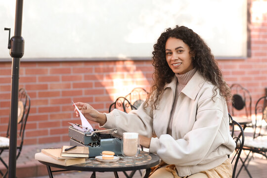 Young African-American author using typewriter at table in street cafe