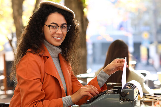 Young African-American author using typewriter at table in street cafe