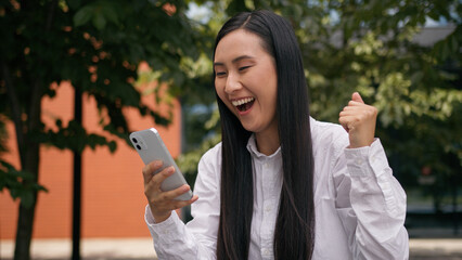 Happy Asian Korean businesswoman woman girl read good news mobile phone smartphone success winning...