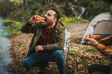 adult man hiker eat hot dog sausage and enjoy while in front tent