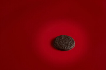 One chocolate cookie illuminated by a beam of light against a red background, chocolate cookie on a...