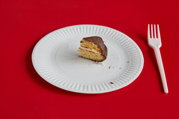 A small piece of chocolate pie on a white disposable plate against a red background with a white disposable fork nearby, a share of the pie, diet.
