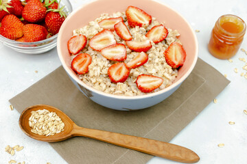 Oatmeal porridge with summer strawberries berries. Porridge oats in bowl with honey,nuts. Healthy food breakfast,lifestyle,dieting, proper nutrition. Top view flat lay on gray table background