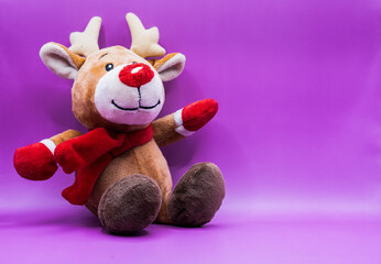 A stuffed reindeer with a red scarf and red mittens is sitting on a purple background