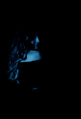 Portrait of a mysterious silhouette of a young woman standing on a blue glowing background