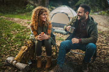 couple eat hot dogs and warm themselves in front campfire