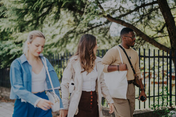 Naklejka premium Three friends walk happily in a lush park, enjoying a day off in nature. They appear relaxed and engaged in conversation, creating a scene of friendship and leisure.