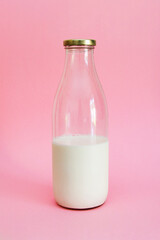 Glass bottle of milk with gold top against a pink background 