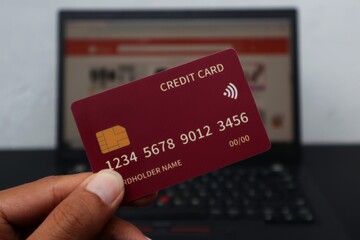 credit card in hand with blurred background online marketplace on laptop