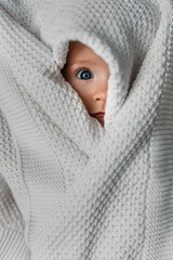 Portrait of a small child covered with a blanket. A beautiful original portrait of a child. The child is under the blanket. A small child peeks out from under the blanket