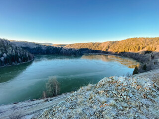 A serene lake, beautifully surrounded by majestic mountains and lush trees, is depicted on a bright...