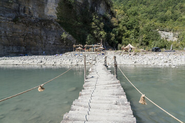 Osumi, Albania - August 15 2024: Handmade rustic wooden bridge (Ura e Vjeter e Zaberzanit) crossing the Osumi River on hot summer day, showcasing traditional Albanian craftsmanship and natural beauty