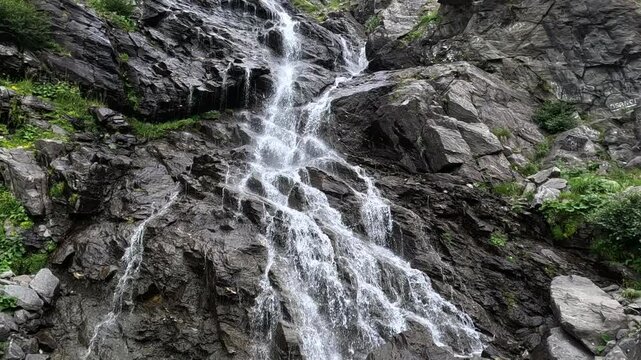 Cascading waterfall flowing over rocky mountainside. Water cascading over a rocky mountainside creates a stunning waterfall, showcasing the beauty of nature. Sunlight glistens on the flowing water