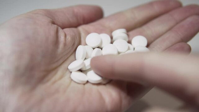 A hand holds a pile of white pills on a white background