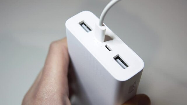 A hand plugs a USB-C cable into a portable power bank