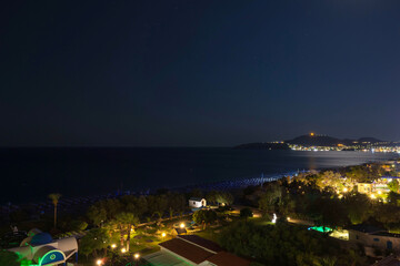 Nighttime coastal view on Rhodes island, Greece, with illuminated beach resort and Aegean Sea.