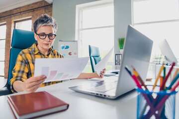 Photo of lovely pensioner lady analyze graph papers dressed plaid yellow shirt comfortable startup office room interior