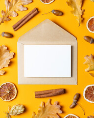Kraft envelope with a blank card on a yellow background, surrounded by autumn leaves, dried orange slices, cinnamon sticks, acorns, and pine cones.