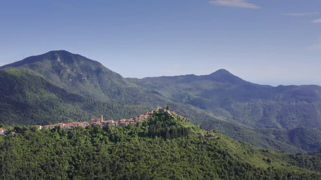 Mountain Village Chuch in Liguria: Drone View of Italy&rsquo;s Green Hills on a Bright Day with Blue Sky &ndash; Wide Shot Drone Flyover Tracking Left