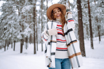 Fototapeta premium Smiling young woman enjoys winter weather at snowy winter park. Boho style. Holidays, rest, travel concept.