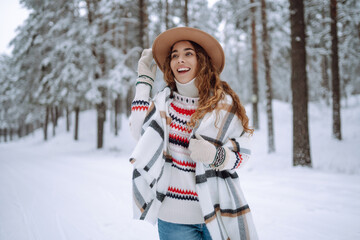 Smiling young woman enjoys winter weather at snowy winter park. Boho style. Holidays, rest, travel concept.