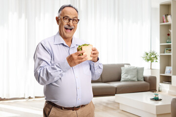 Elderly man holding a sandwich and smiling at home