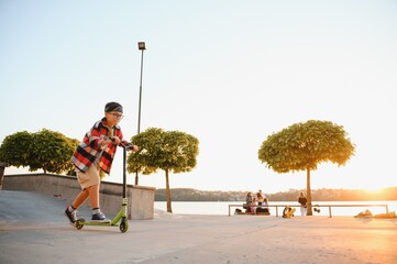 teenage boy has fun riding his push scooter at the skate park © Serhii