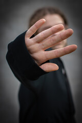 Obraz premium gesture of categorical refusal. palm extended forward. caucasian girl on gray background with vignette. artistic vertical photo with selective focus on hand