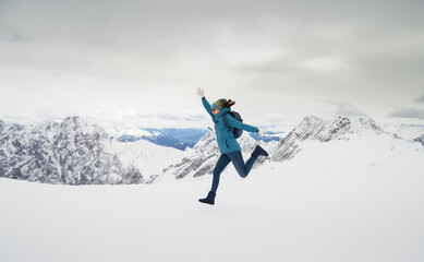 a woman in a blue jacket jumps against the backdrop of snow-capped mountains, winter in the mountains