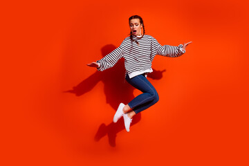 Obraz premium Charismatic young woman jumps against a vibrant orange backdrop showcasing casual fashion in striped pullover