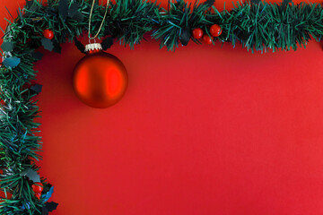 Festive Christmas decorations, garland with red berries and a red ball christmas tree ornament on a red background copyspace for season, Christmas or New Year greetings.