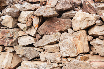 A wall constructed of medium sized stones, arranged one atop the other, featuring a blend of cream...