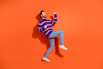 Cheerful young man in striped sweater dancing against vibrant orange wall with joyful expression