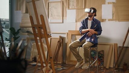 A Male Artist Uses VR Glasses to Create Unique Art in His Bright Studio, Surrounded by His Finished...