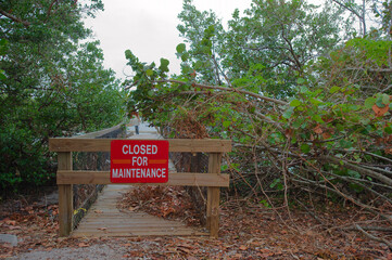 Red Closed for maintenance sign on nature trail wood park boardwalk Looking out with green trees...