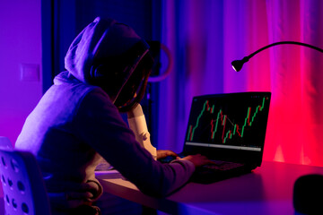 Young male trading stocks online in funky illuminated room