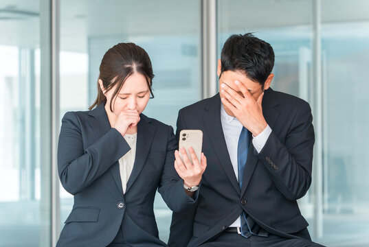 スマホ・スマートフォンを見てショックを受ける会社員（炎上・トラブル・失敗・カスハラ・困る）
