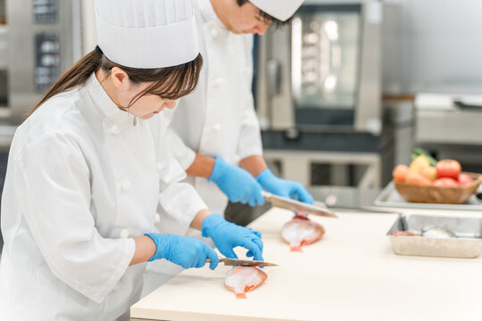 魚を調理するコックコート姿の男女スタッフ（調理師・専門学校・料理人・生鮮市場・食品加工）

