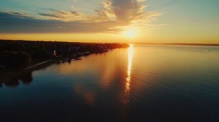 Fototapeta premium A serene sunset over a calm lake, reflecting golden hues and clouds, creating a tranquil atmosphere.