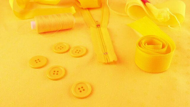 Cotton fabric and various sewing accessories in merigold yellow colors rotates on the showcase. Sewing zipper, buttons, threads, floss, yarn, satin ribbon. 
