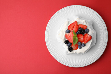 Pavlova cake (meringue dessert) with whipped cream, fresh berries and mint on red background, top view. Space for text