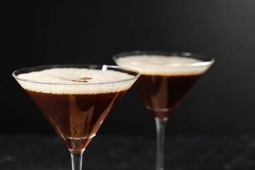 Delicious espresso martini in glasses on blurred black background, closeup