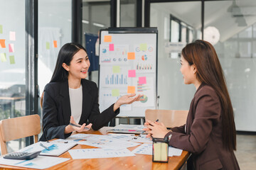 Professional women discussing business strategies in modern office. They are engaged in conversation with charts and documents on table, showcasing teamwork and collaboration
