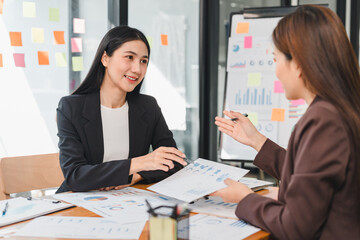 Professional women discussing business strategies in modern office. They are engaged in collaborative meeting, analyzing charts and graphs on documents