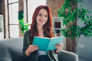 Fototapeta premium Photo of attractive young ginger woman reading interesting book dressed khaki outfit cozy day light home interior living room