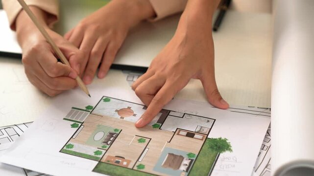 Smart architect and safety engineer discussion about building blueprint on table with architectural document, measurement tools and wooden block scatter around at modern office. Closeup. Delineation.
