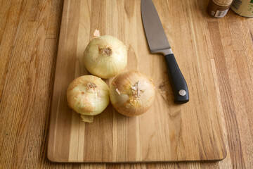 Ripe raw onions on a wooden cutting board with a chef's knife.