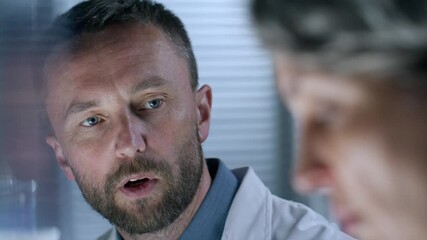 Male laboratory technician in white coat discussing results of scientific research with female colleague. Close-up shot